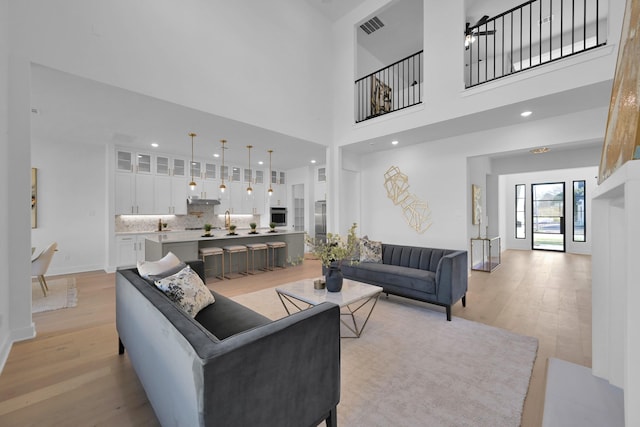 living area with visible vents, recessed lighting, light wood-style floors, a high ceiling, and baseboards