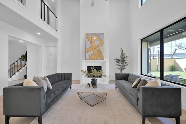 living room featuring a fireplace, a ceiling fan, stairs, and baseboards