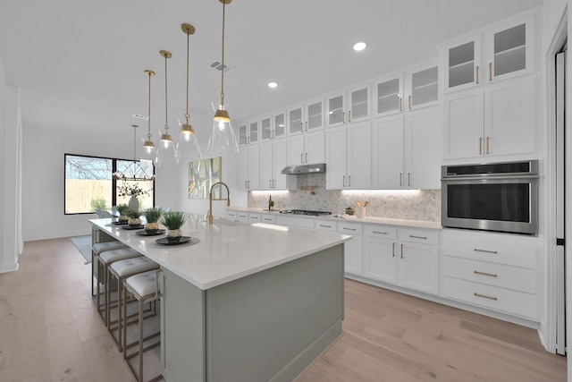 kitchen with visible vents, under cabinet range hood, a sink, tasteful backsplash, and stainless steel oven