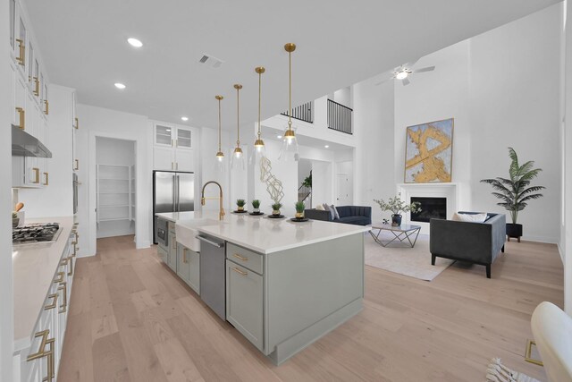 kitchen with under cabinet range hood, light wood-style floors, a glass covered fireplace, white cabinetry, and a sink