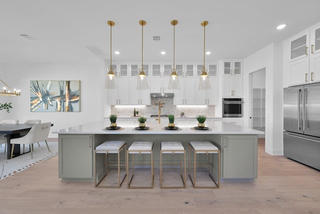 kitchen with tasteful backsplash, visible vents, under cabinet range hood, light wood-type flooring, and appliances with stainless steel finishes