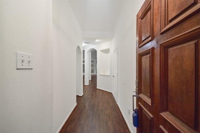 hallway featuring dark wood-style floors, arched walkways, and baseboards