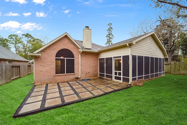 back of house featuring a sunroom, a fenced backyard, a chimney, a yard, and brick siding