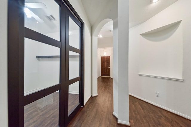 hall with arched walkways, visible vents, baseboards, and wood finished floors