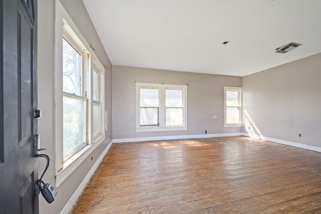 spare room featuring a wealth of natural light, wood finished floors, visible vents, and baseboards