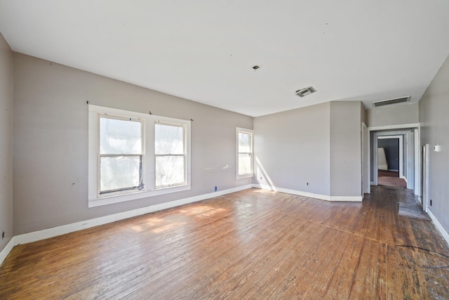 empty room featuring hardwood / wood-style flooring, visible vents, and baseboards