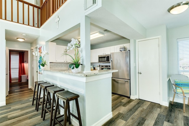 kitchen with white cabinetry, appliances with stainless steel finishes, a breakfast bar area, and wood finished floors