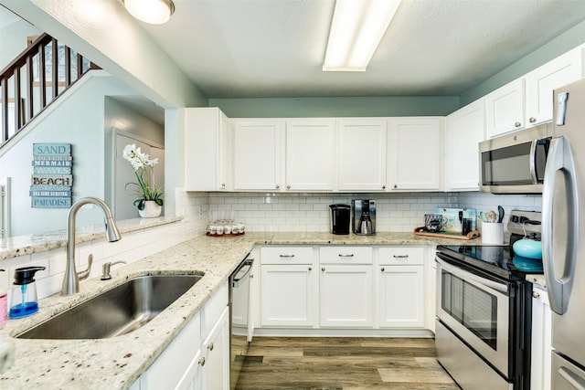 kitchen with appliances with stainless steel finishes, white cabinets, a sink, and wood finished floors