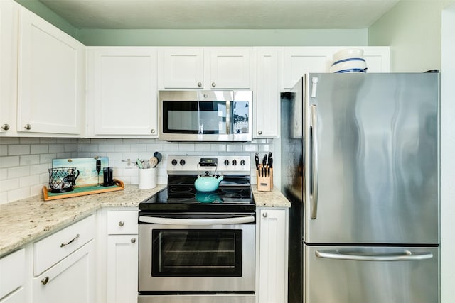 kitchen featuring stainless steel appliances, white cabinets, backsplash, and light stone countertops