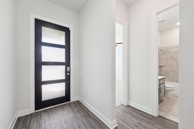 foyer entrance featuring baseboards, visible vents, and wood finished floors