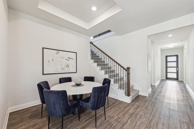 dining space with recessed lighting, a raised ceiling, wood finished floors, baseboards, and stairs