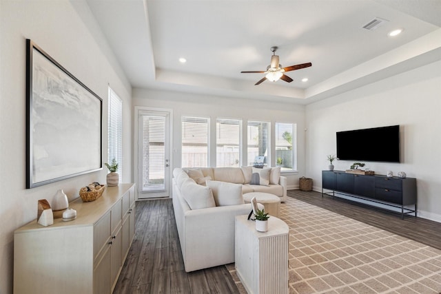 living area featuring wood finished floors, a raised ceiling, visible vents, and baseboards