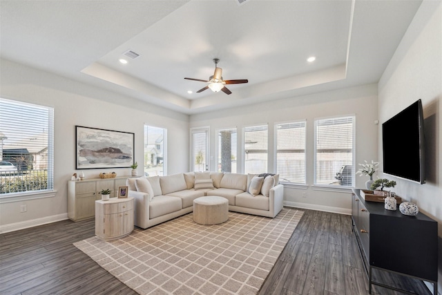 living room with a tray ceiling, recessed lighting, baseboards, and wood finished floors