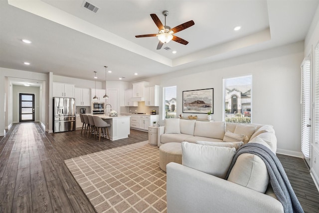 living room featuring a raised ceiling, visible vents, dark wood finished floors, and baseboards