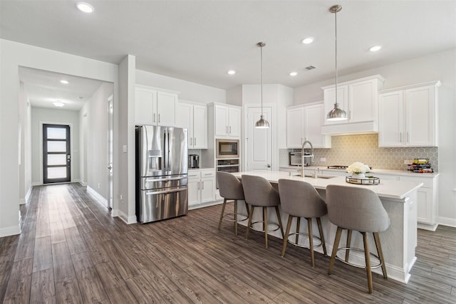 kitchen with stainless steel appliances, dark wood finished floors, a center island with sink, and a kitchen bar