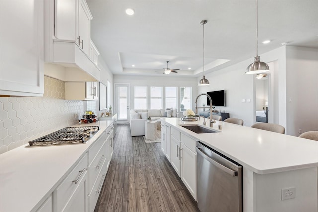 kitchen with stainless steel appliances, a sink, open floor plan, decorative backsplash, and a raised ceiling