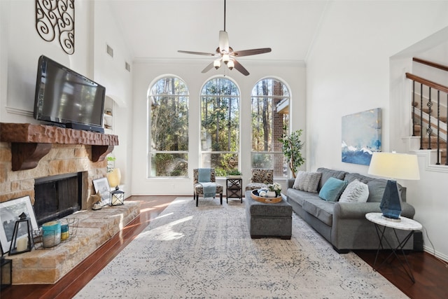 living room featuring visible vents, a ceiling fan, wood finished floors, crown molding, and a stone fireplace