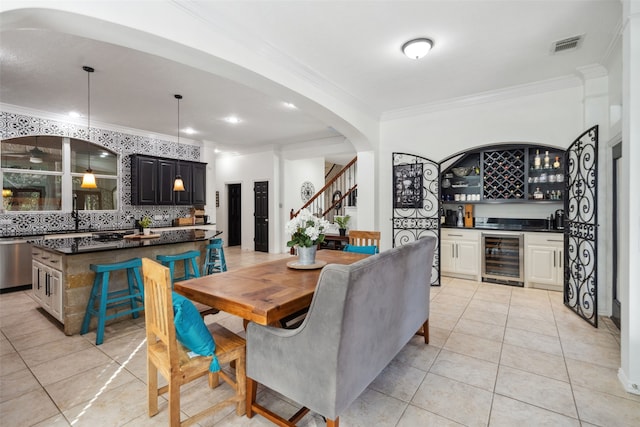 dining space with light tile patterned floors, arched walkways, beverage cooler, ornamental molding, and a dry bar