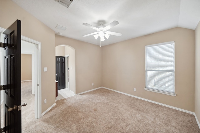 carpeted empty room with arched walkways, ceiling fan, lofted ceiling, visible vents, and baseboards