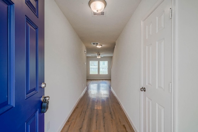 hall with visible vents, baseboards, and wood finished floors