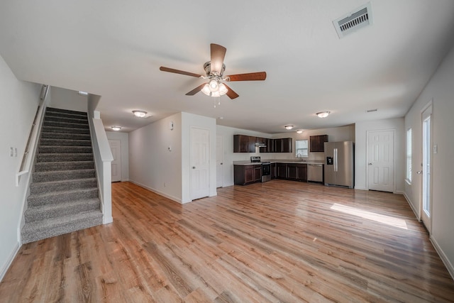 unfurnished living room featuring light wood-style flooring, visible vents, stairway, and baseboards