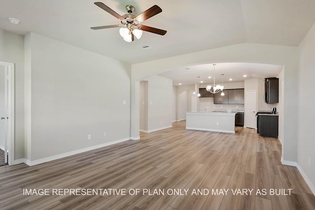 unfurnished living room with arched walkways, light wood-style flooring, ceiling fan with notable chandelier, visible vents, and baseboards