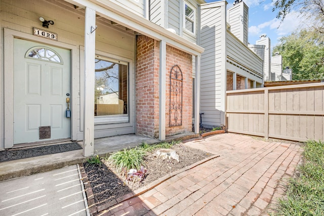 view of exterior entry featuring brick siding and fence