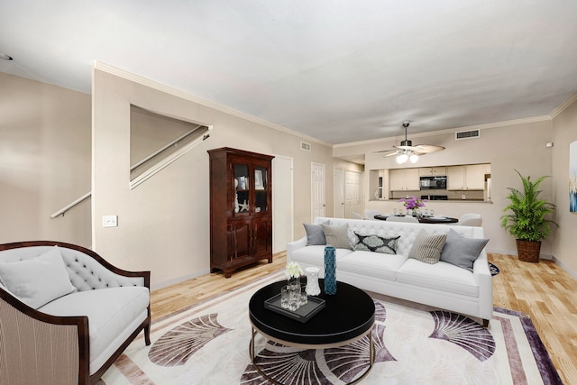 living room featuring ceiling fan, ornamental molding, visible vents, and light wood-style floors