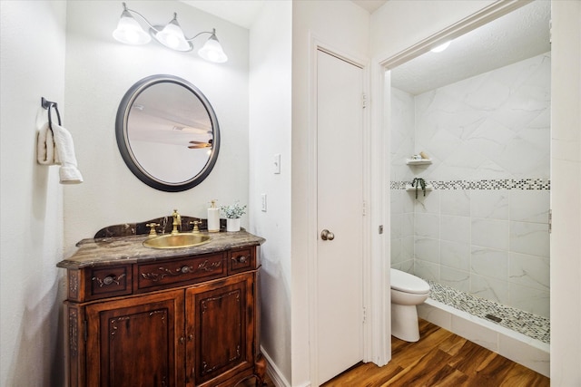 full bath with toilet, tiled shower, wood finished floors, and vanity