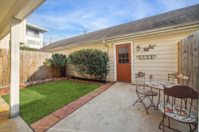 entrance to property featuring a shingled roof, a lawn, a patio area, and fence