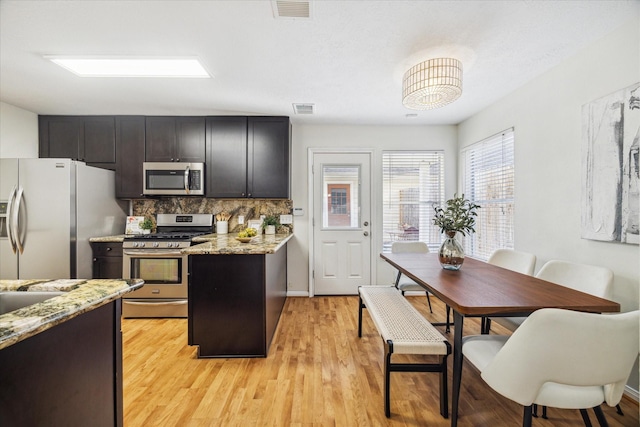 kitchen featuring light stone counters, visible vents, light wood-style floors, appliances with stainless steel finishes, and decorative backsplash