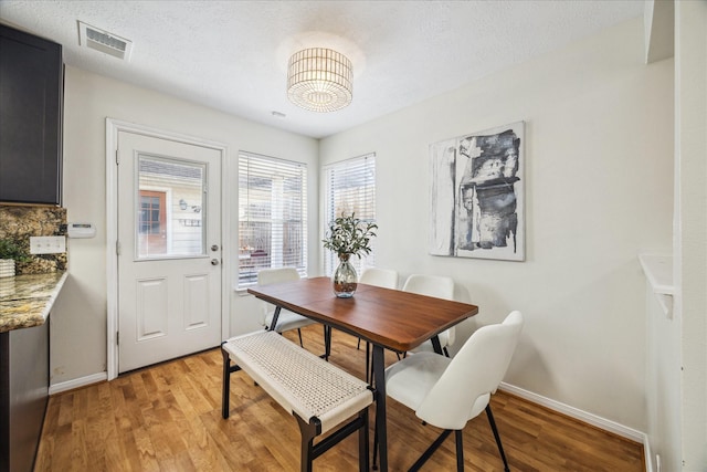 dining room featuring light wood-style floors, visible vents, a textured ceiling, and baseboards