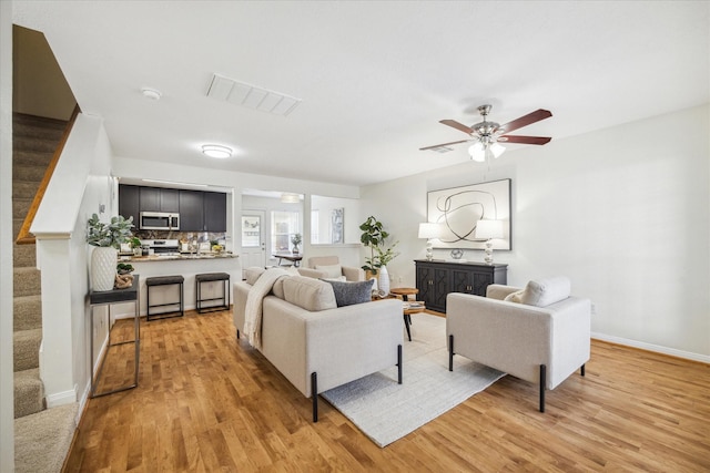 living area featuring stairs, light wood finished floors, visible vents, and a ceiling fan