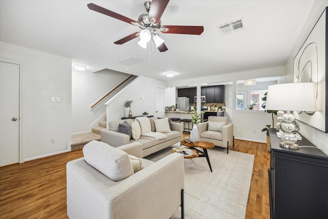 living room with a ceiling fan, wood finished floors, visible vents, and stairs