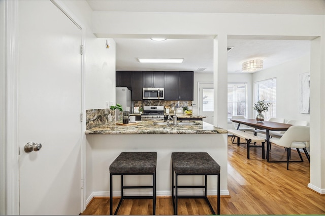 kitchen with backsplash, appliances with stainless steel finishes, light wood-style floors, a sink, and a peninsula