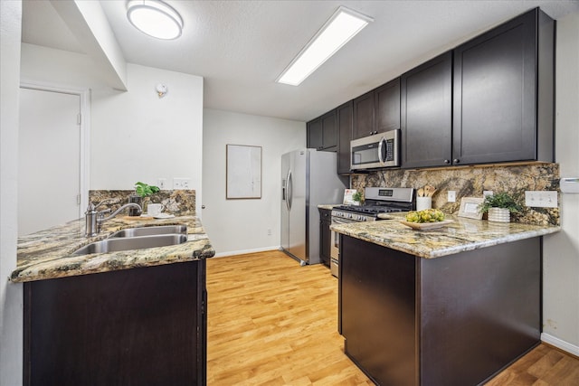 kitchen featuring light stone counters, stainless steel appliances, light wood-style floors, a sink, and a peninsula