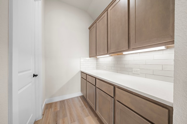 9975 Monarch Landing Cv, Willis, TX 77318 - kitchen with light wood-type flooring, decorative backsplash, light countertops, vaulted ceiling, and baseboards