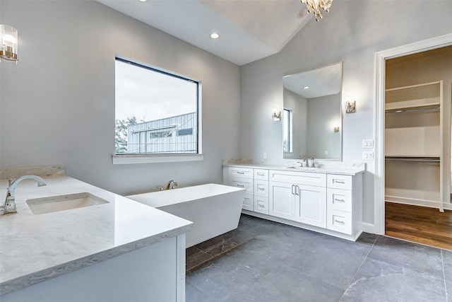 bathroom featuring vaulted ceiling, a soaking tub, two vanities, and a sink