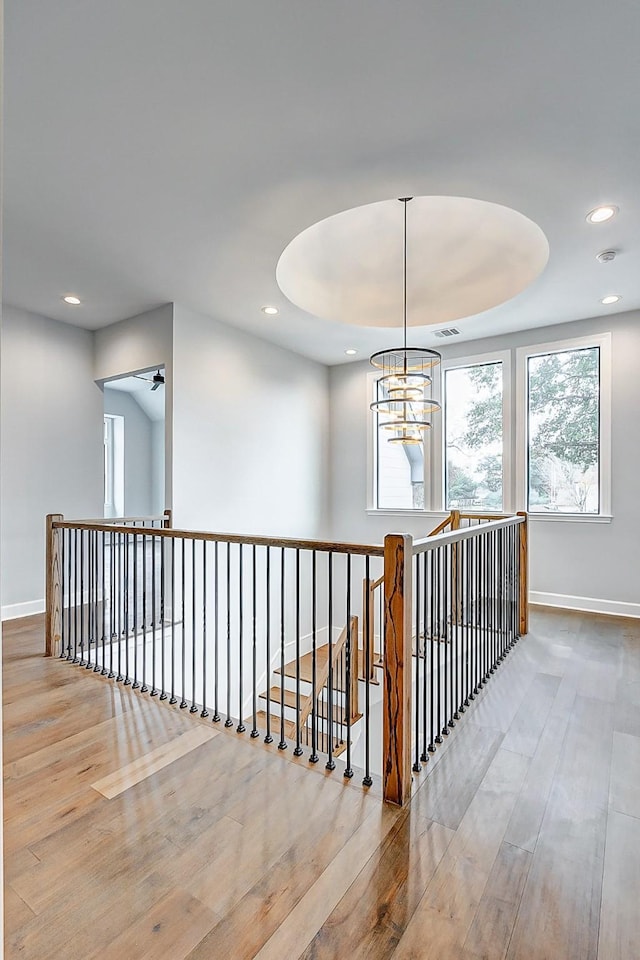 hallway featuring a raised ceiling, visible vents, wood finished floors, a chandelier, and baseboards