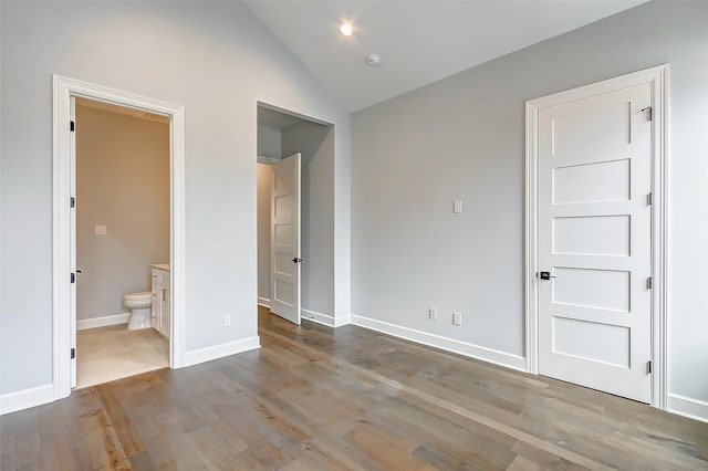 unfurnished bedroom featuring baseboards, lofted ceiling, wood finished floors, ensuite bathroom, and recessed lighting