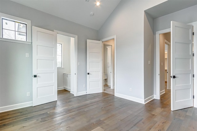 unfurnished bedroom with multiple windows, vaulted ceiling, and wood finished floors