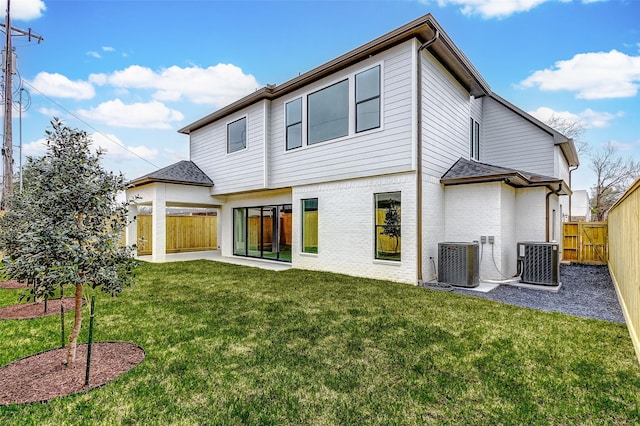 rear view of house with a yard, a fenced backyard, central AC, and brick siding