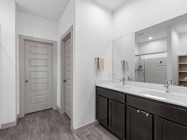 bathroom featuring double vanity, a sink, a shower stall, and wood finished floors