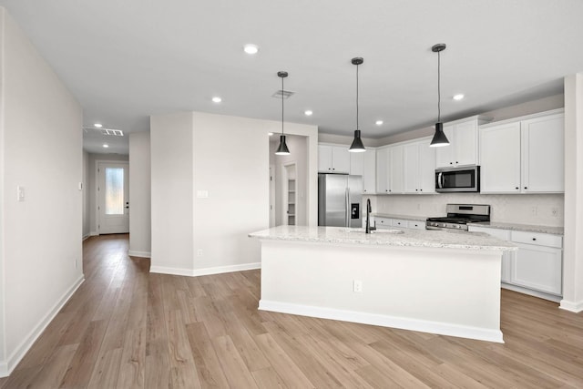 kitchen featuring appliances with stainless steel finishes, light wood-style floors, white cabinets, a sink, and a kitchen island with sink