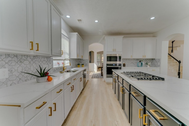 kitchen with arched walkways, a sink, visible vents, white cabinets, and appliances with stainless steel finishes