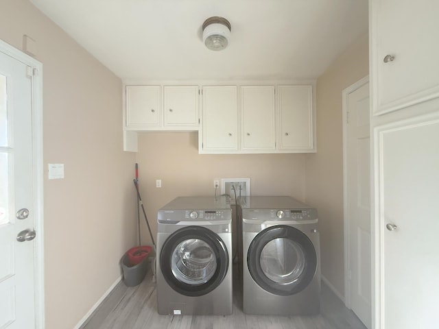 clothes washing area with washer and clothes dryer, cabinet space, light wood-style flooring, and baseboards