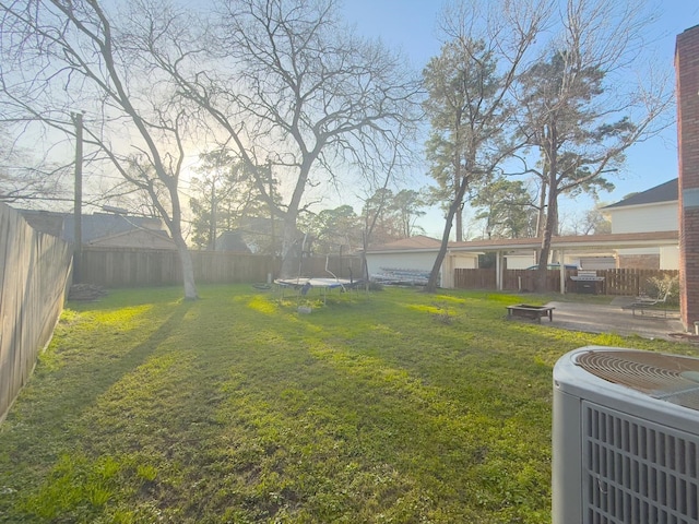 view of yard with a trampoline, central AC unit, and a fenced backyard