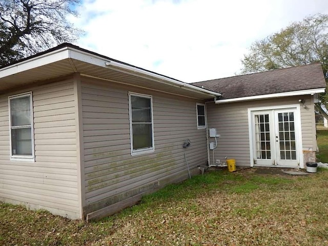 view of side of property featuring a yard, french doors, and a shingled roof