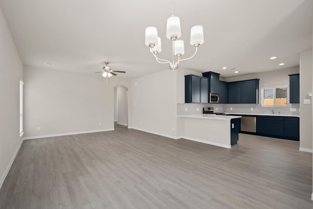 kitchen with arched walkways, ceiling fan with notable chandelier, open floor plan, light countertops, and appliances with stainless steel finishes