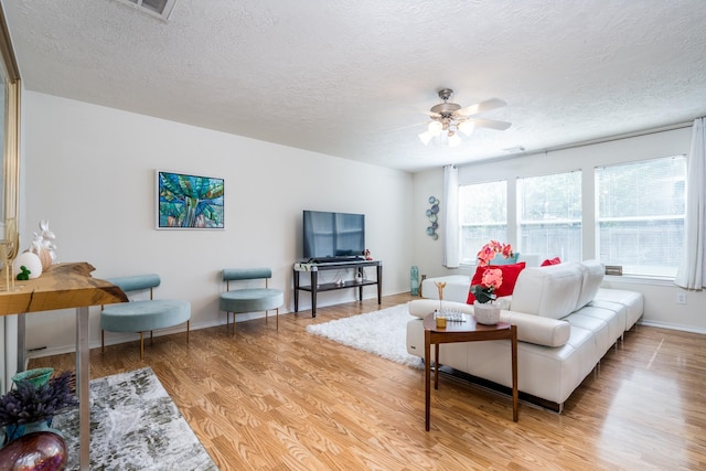 living room with a ceiling fan, light wood-type flooring, a textured ceiling, and baseboards